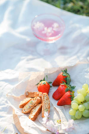 Spring picnic in nature. A glass of pink champagne with sakura flowers, a wicker bag, a hat, Italian.の写真素材