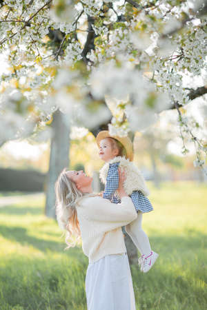 A beautiful young mother with her little daughter are resting on a picnic in the flowering garden. White flowers. Spring.の写真素材