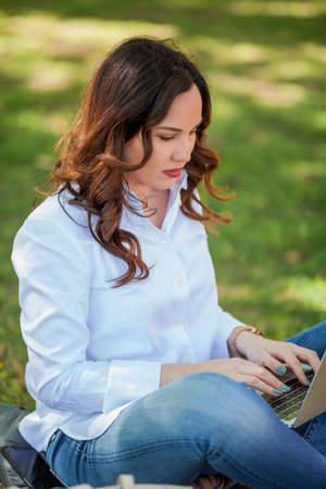 Young happy woman works at a laptop in nature. Quarantine. Freelancer. City.の写真素材