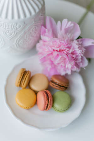 Living room interior. Bouquet of pink peonies in a vase, multicolored French macaroon pastries....
