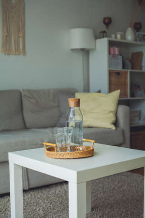 Home interior. A glass bottle with water, a glass, a rattan wicker tray on a coffee table. Cozy.の写真素材