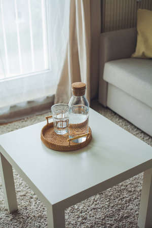 Home interior. A glass bottle with water, a glass, a rattan wicker tray on a coffee table. Cozy.の写真素材