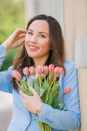 Portrait of a beautiful young woman in a blue suit with a bouquet of tulips.の写真素材