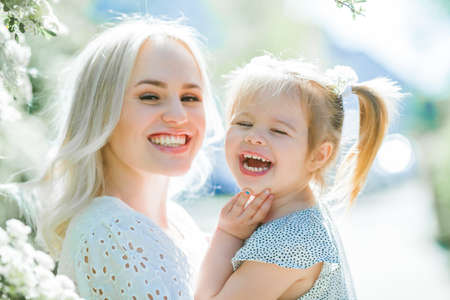 A beautiful young mother with her daughter 3 years old in a blooming garden. Spring.の写真素材