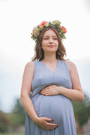 Portrait of a young pregnant woman with a wreath on her head in the park. Pregnancy.の写真素材