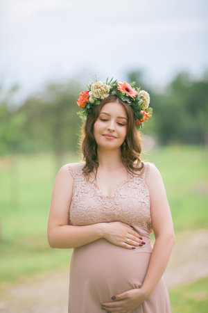 Portrait of a young pregnant woman with a wreath on her head in the park. Pregnancy.の写真素材