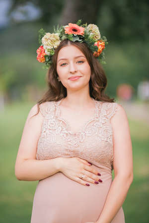 Portrait of a young pregnant woman with a wreath on her head in the park. Pregnancy.の写真素材