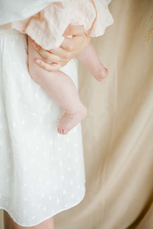 A young beautiful mother in a white dress is breastfeeding her little daughter, 5 months old, sitting in a chair by the window.の写真素材