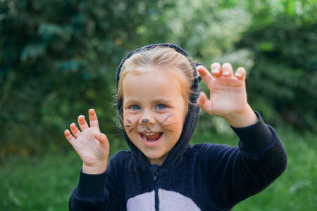 Cute girl in a plush cat costume holds a pumpkin-shaped candy bucket in her hands. Halloween.の写真素材
