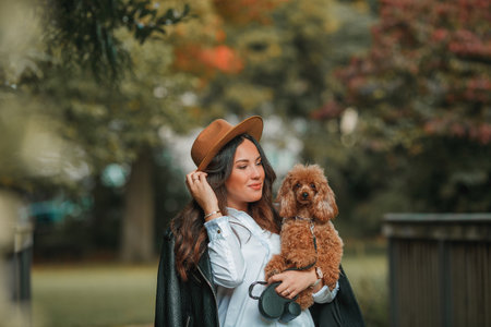 A beautiful young dark-haired woman walks in the park and hugs her poodle dog. Autumn mood. Fall.の写真素材