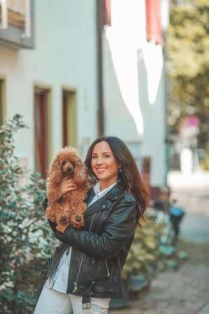 A young beautiful woman with her poodle dog is walking in a European city. Happiness. Little pet. Fall.の写真素材
