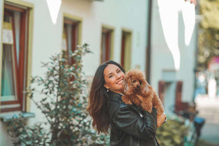 A young beautiful woman with her poodle dog is walking in a European city. Happiness. Little pet. Fall.の写真素材