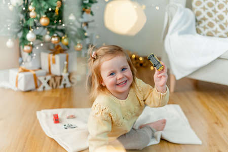 Adorable little blue eyed girl in knitted pullover at the Christmas tree. holiday atmosphere. Cozy.の写真素材