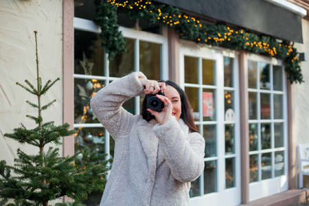 Beautiful young dark haired woman tourist in beige eco-coat makes Christmas photo on European...