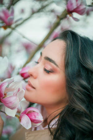 Spring portrait of young dark haired curly woman near blooming magnolia. Emotional model near tree with pink flowers. Warm season. Holidays.の写真素材