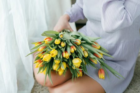 Spring portrait of beautiful dark haired curly woman in lilac dress with large color bouquet of tulips at home. Emotional model holds flowers in her hands. Women's Day. present. mother's day.の写真素材