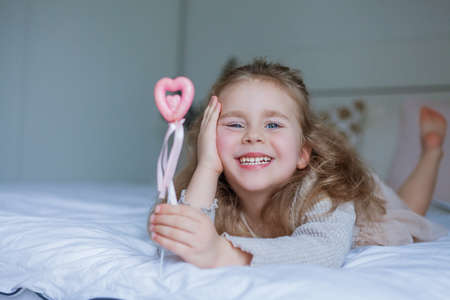 Cute little blue-eyed girl holds a pink little heart in her hands. Happy child gives a gift. Valentine's Day. home.の写真素材