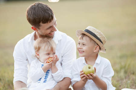 Beautiful dad and his two little children in light natural clothes a boy and a girl on a picnic on a summer evening in a field. happy parenting. freedom.の写真素材
