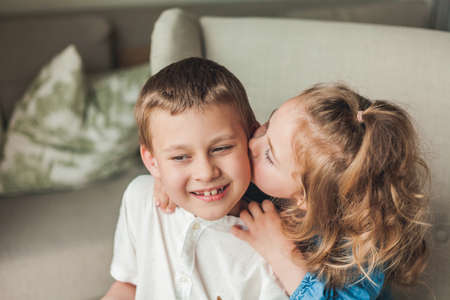 Portrait of little happy children brother and sister sitting in a cozy armchair in a bright house. family relationships.の写真素材