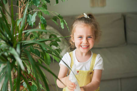 Cute blue-eyed curly-haired girl of 4 years old pours houseplants with water from a watering can in a cozy house. Little child helps his mother with household chores. Eco friendly. Planet.の写真素材