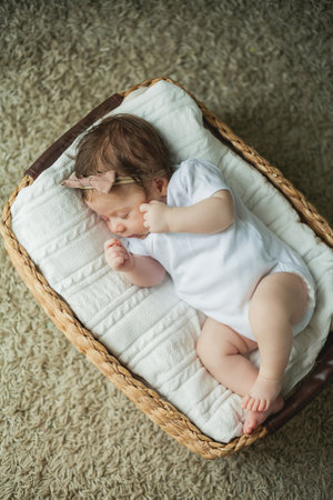 Close portrait of a cute baby 2 months old girl in white clothes in a wicker basket. home.の写真素材