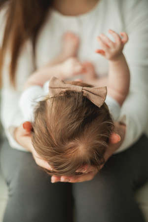Close portrait of a little cute dark-haired newborn girl in a white suit in the arms of a young mother. motherhood. parent. Healthy sleep. home.の写真素材