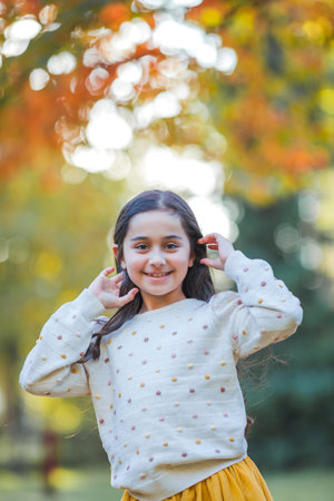 Portrait of a little beautiful girl of 9 years old with long dark hair in bright clothes. happy child in autumn park. fall.の写真素材