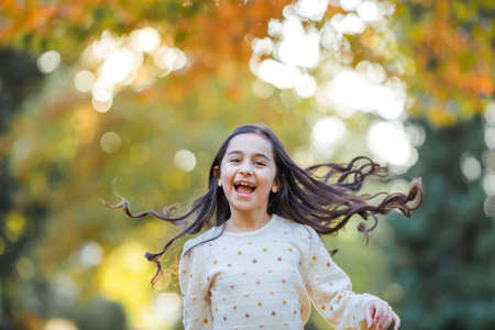 Portrait of a little beautiful girl of 9 years old with long dark hair in bright clothes. happy child in autumn park. fall.の写真素材