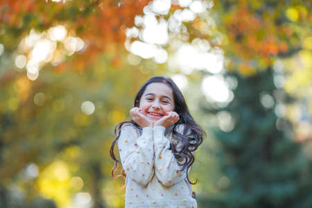 Portrait of a little beautiful girl of 9 years old with long dark hair in bright clothes. happy child in autumn park. fall.の写真素材