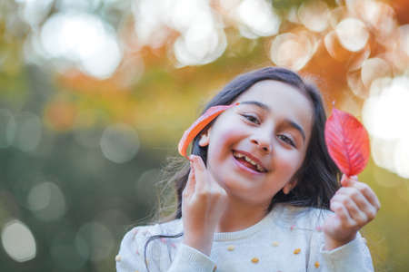 Portrait of a little beautiful girl of 9 years old with long dark hair in bright clothes. happy child in autumn park. fall.の写真素材