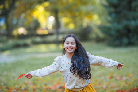 Portrait of a little beautiful girl of 9 years old with long dark hair in bright clothes. happy child in autumn park. fall.の写真素材