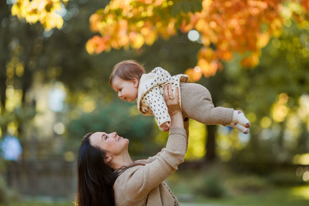 Beautiful young mother with a cute little girl 7 months old walks in the autumn park. Portrait of a happy family.の写真素材