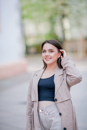 Young beautiful woman 19 years old in stylish clothes. Model with dark hair in casual clothes walks through the spring blooming city.の写真素材