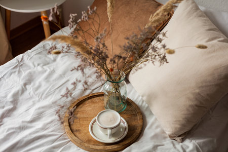 Hot mug of cappuccino on wooden tray on the bed, breakfast, bouquet of dried flowers. spring scenery. Cozy house.の写真素材