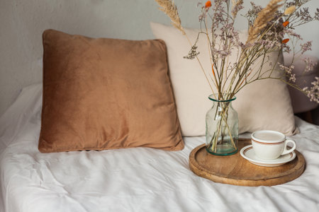 Hot mug of cappuccino on wooden tray on the bed, breakfast, bouquet of dried flowers. spring scenery. Cozy house.の写真素材