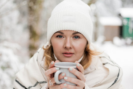 Portrait of young woman in warm clothes in winter forest. Drinking hot tea outdoors from flask. Hiking.の写真素材