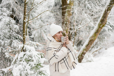 Portrait of young woman in warm clothes in winter forest. Drinking hot tea outdoors from flask. Hiking.の写真素材