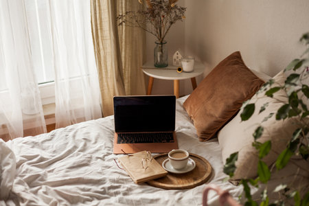 Cup of hot cappuccino, a book, glasses, a laptop on the bed. Work online at home. home office.の写真素材