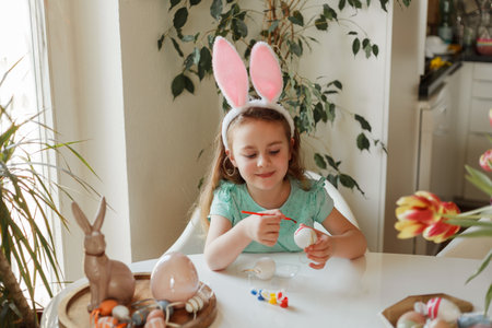 Easter. A cute little girl in bunny ears decorates Easter eggs at the table at home. Spring.の写真素材