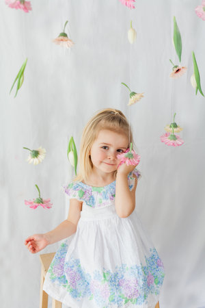 Cute little girl 3 years old with blond hair with colored flowers on white background. Spring. holidays.の写真素材
