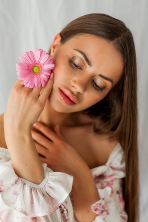 Portrait of young beautiful long-haired brown-eyed woman with pink gerbera on white background. Spring. holidays.の写真素材