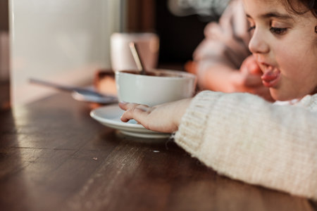 Beautiful young red-haired mother with cute curly-haired daughter are sitting in cozy cafe and drinking hot school. mother's day.の写真素材