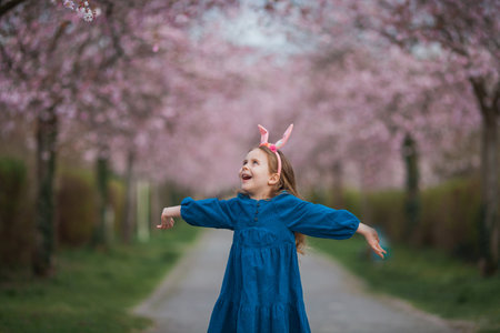 Easter. Little cute girl with long curly hair with bunny ears in cherry blossoms. Spring.の写真素材