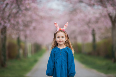 Easter. Little cute girl with long curly hair with bunny ears in cherry blossoms. Spring.の写真素材