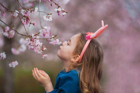 Easter. Little cute girl with long curly hair with bunny ears in cherry blossoms. Spring.の写真素材