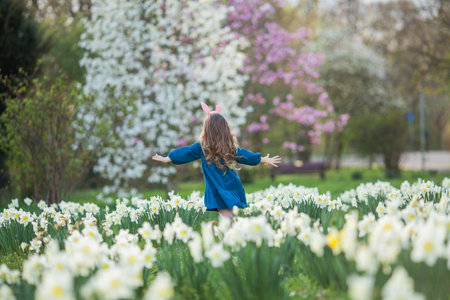 Easter. Little cute girl 5 years old with rabbit ears on the lawn of daffodils. happy child.の写真素材