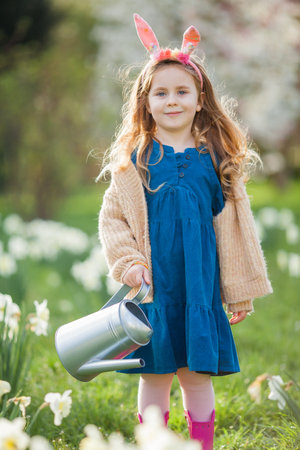 Easter. Cute little girl of 5 years old with rabbit ears is watering daffodils on the lawn. happy child.の写真素材