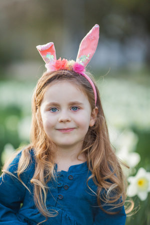 Easter. Little cute girl 5 years old with rabbit ears on the lawn of daffodils. happy child.の写真素材