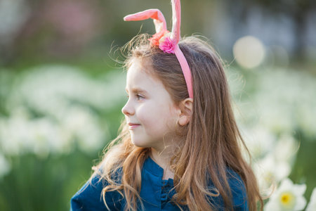 Easter. Little cute girl 5 years old with rabbit ears on the lawn of daffodils. happy child.の写真素材