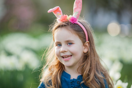 Easter. Little cute girl 5 years old with rabbit ears on the lawn of daffodils. happy child.の写真素材